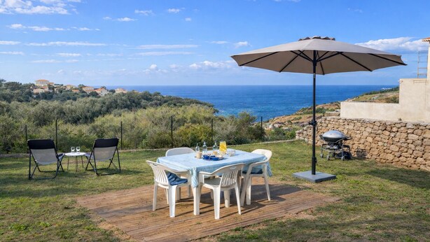 Een buitenterras met een tafel, stoelen, een grote parasol en uitzicht op zee.
