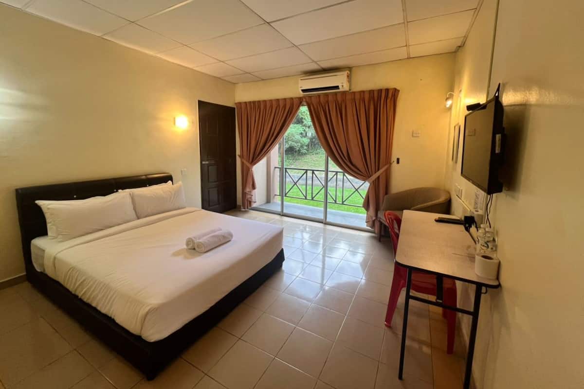 A hotel room with a bed, a desk, a chair, a television, and a sliding glass door to the outside.