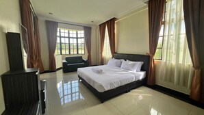 Una habitación de hotel con cama, televisor, sofá y ventanas grandes con cortinas.