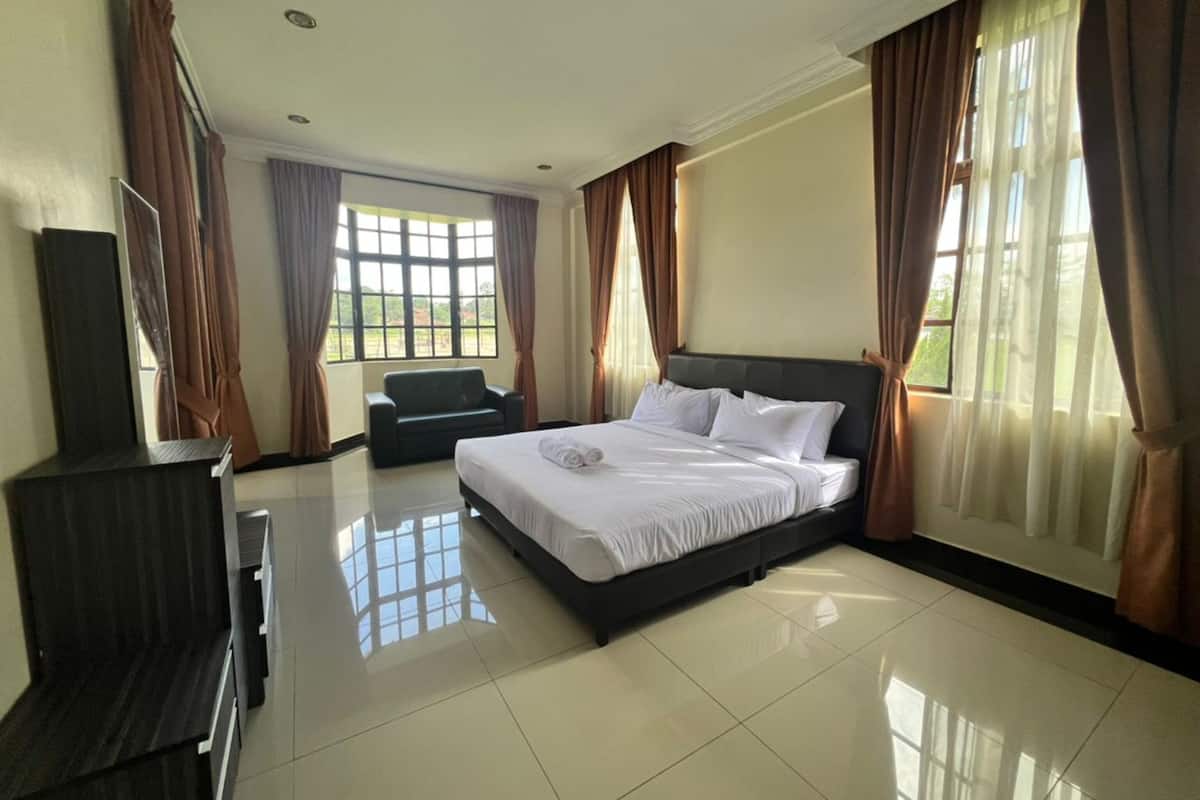 A hotel room with a bed, a TV, a sofa, and large windows with curtains.