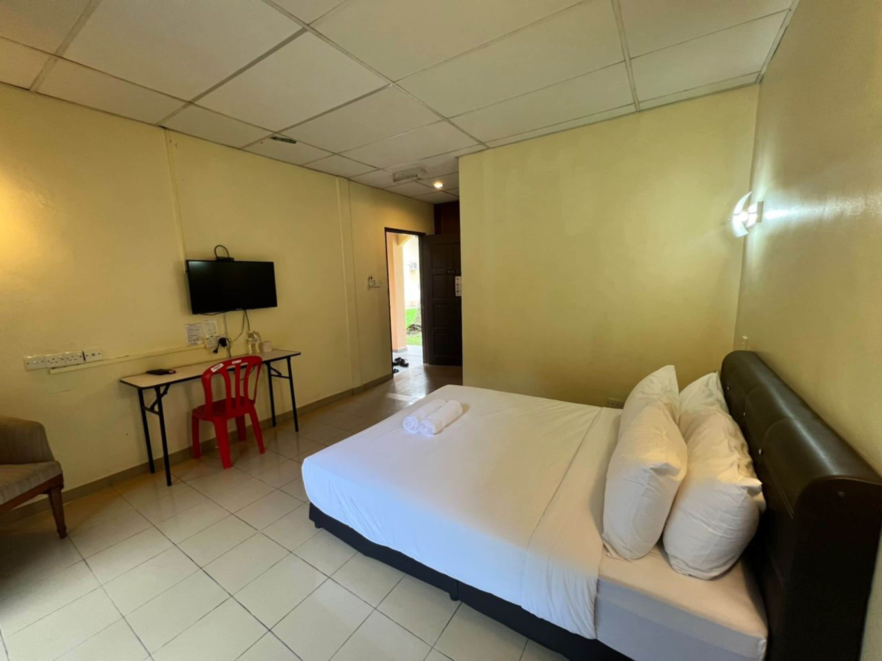 A hotel room with a bed, a desk with a chair, a television, and a door leading to a balcony.