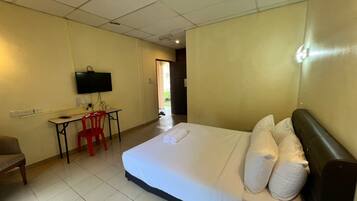 A hotel room with a bed, a desk with a chair, a television, and a door leading to a balcony.