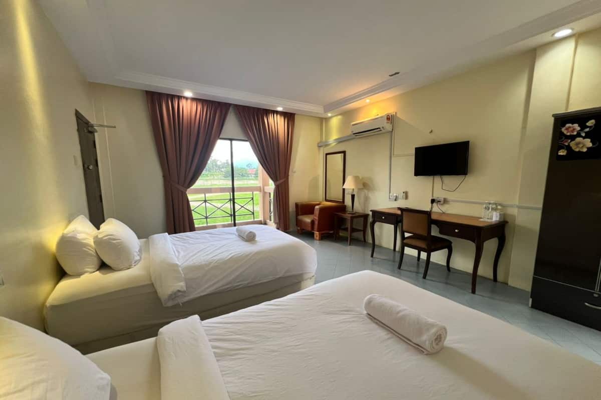 A hotel room with two beds, a desk, a chair, a TV, and an air conditioning unit.