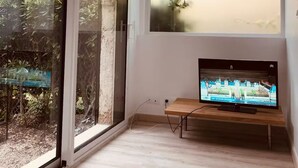 A modern living room with a large sliding glass door, a television on a wooden stand, and a view of greenery outside. - Carry le Rouet - Relaxation and vacations with your feet in the water  (Carry-le-Rouet)