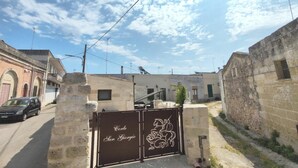 Una entrada con reja que muestra un emblema de un caballo y jinete, edificios de piedra y cielo despejado.