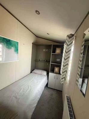 A compact bedroom with a single bed, built-in storage, a mirror, and a partial view of a bathroom. - Flagshipsite-caravan-sleeps7-fast Internet (Rhyl)