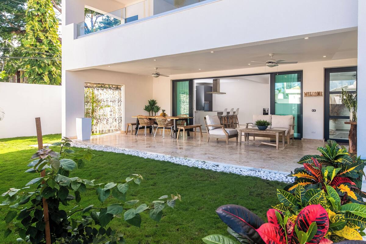 A modern house with a patio, outdoor seating, and a well-maintained lawn.
