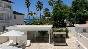 A pool area with lounge chairs and umbrellas, a covered seating area, and a view of the ocean and palm trees. - Stella Apart-hotel Las Terrenas (Las Terrenas)