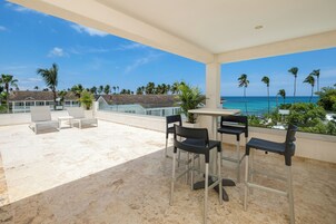 Una terraza en la azotea con mesa y sillas, con vistas a una playa y palmeras.