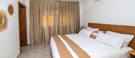 A neatly made bed with white and brown bedding, a ceiling fan, and an air conditioning unit on the wall.