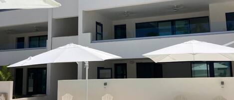 A modern multi-story building with a swimming pool, outdoor seating, and a clear blue sky.
