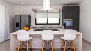 A modern kitchen with a central island, white bar stools, and built-in appliances. - Stella Apart-hotel Las Terrenas (Las Terrenas)