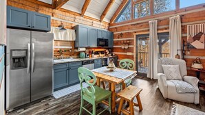 A rustic cabin interior with a wooden dining table, chairs, a refrigerator, and a kitchen area with cabinets and a microwave. - Mountain View Cabin with Hot Tub, Outdoor Theater and King Bed (Townsend)