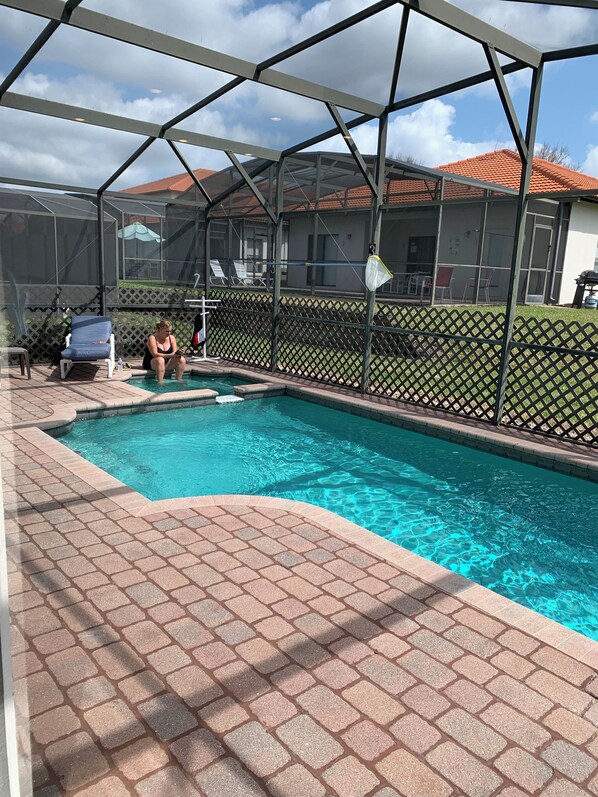 A swimming pool with a covered area, a fenced patio, and a view of a house with a red roof.
