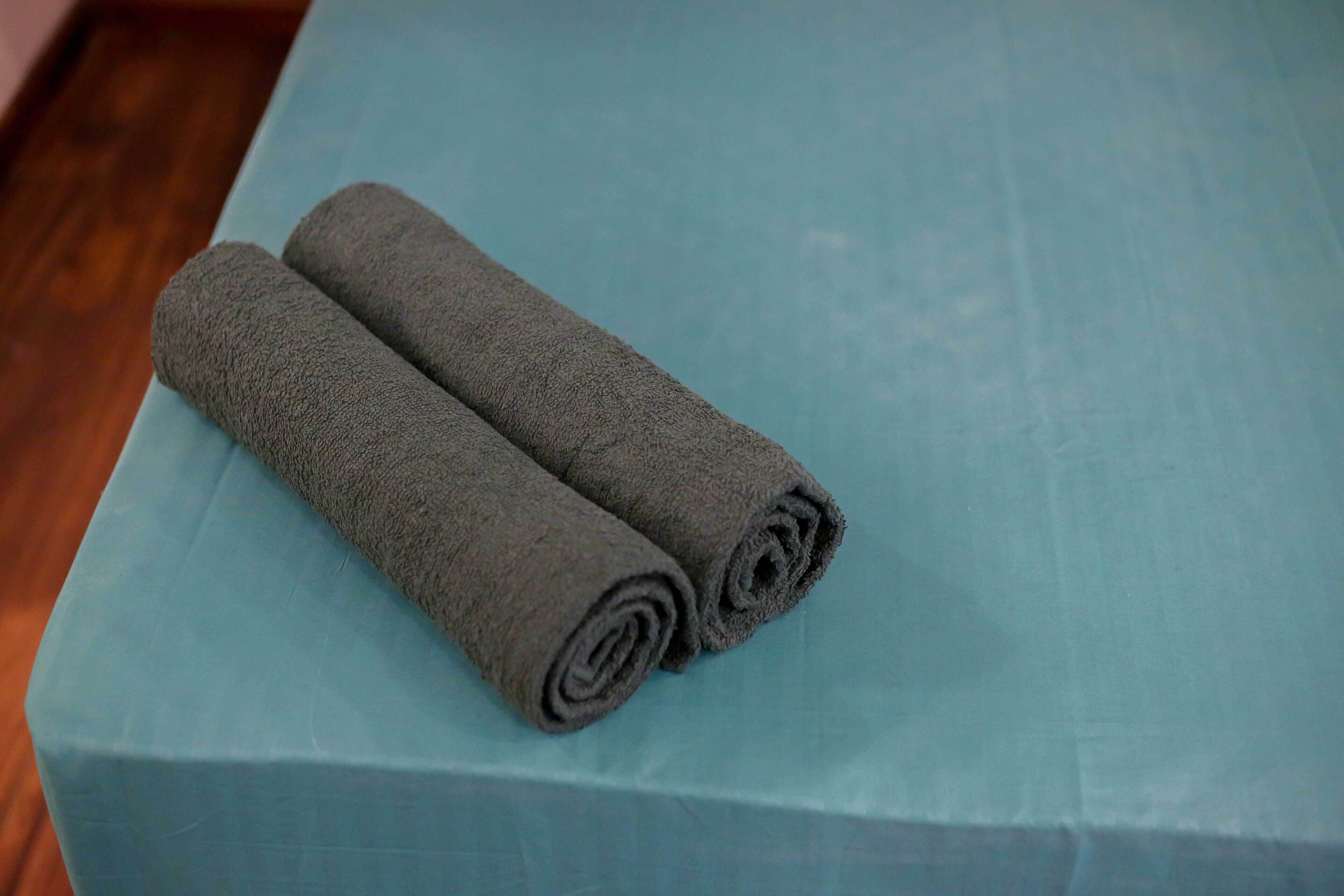 A blue bed with two rolled-up gray towels placed on it.