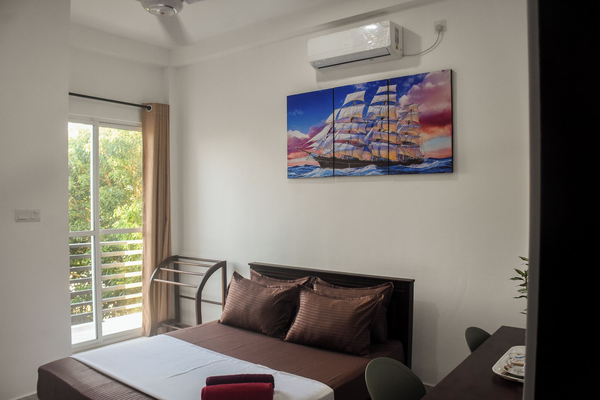 Ein Hotelzimmer mit Bett, einem Segelschiff-Gemälde, einem Vorhangfenster und einer Klimaanlage.