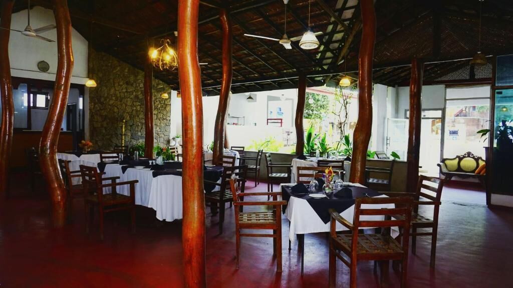 Un comedor interior con pilares de madera, mesas con manteles blancos y sillas.