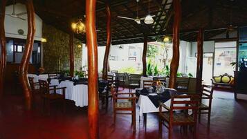 Un comedor interior con pilares de madera, mesas con manteles blancos y sillas.