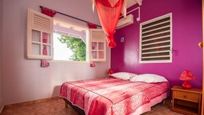 A bedroom with a bed, a window with curtains, a nightstand, and a wall-mounted air conditioning unit.