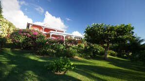 A house with a covered porch, surrounded by lush greenery and flowering plants.