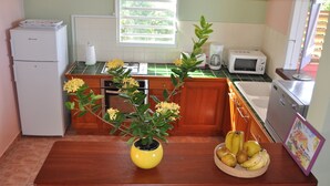 A kitchen with a refrigerator, microwave, toaster, and a sink. There is a wooden counter with a vase of flowers and a basket of fruit.