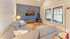 Una sala de estar con un sofá gris, una mesa de centro de madera, una pared azul, una chimenea y una estantería.