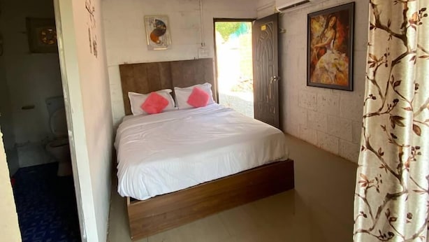 A bedroom with a bed, a painting, and a door. - Khushi Resort Pernem (Mandrem)