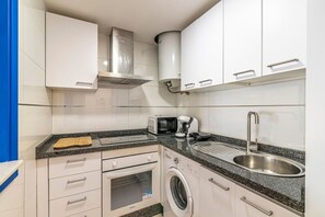 Una cocina compacta con armarios blancos, un lavamanos de acero inoxidable, un microondas, un tostador y una lavadora.