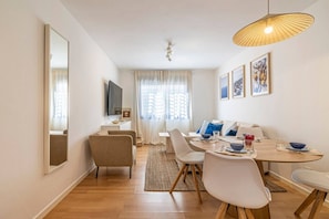 A modern dining area with a round table, chairs, and a television on a stand. - Solis Mare - Pedregalejo Beach (Málaga)