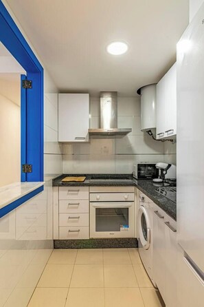 A compact kitchen with white cabinets, a built-in oven, a microwave, and a washing machine.