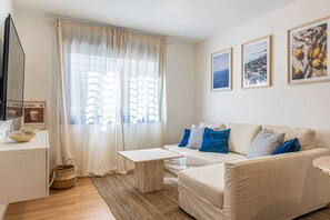 Una sala de estar con sofá, mesa de centro, televisor y ventana con cortinas.