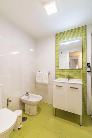 A bathroom with a toilet, bidet, sink, and mirror.
