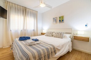 Habitación de hotel con cama, cortinas, televisor de pantalla plana, dos cuadros colgados en la pared y una mesita de noche con lámpara.