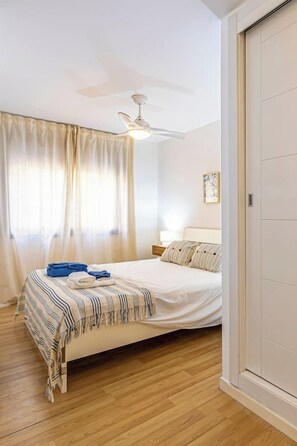 A bedroom with a bed, curtains, a ceiling fan, and a bedside table.