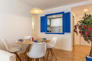 A dining area with a round table, white chairs, and a blue-framed mirror above the kitchen.