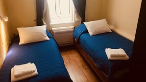A small room with two beds, each with a blue bedspread and white pillows. There is a window with curtains, a heater on the floor, and a towel on each bed. - Spacious 3 apartment , villa with WiFi and AC in delightful Dobrota (Dobrota)