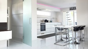 A modern kitchen with white cabinetry, a stainless steel range hood, and a glass dining table with metal chairs. - Ringö Resort (Gothenburg)
