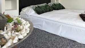 A modern bedroom with a large bed, a dark headboard, and a small bedside table with a plant. - Ringö Resort (Gothenburg)