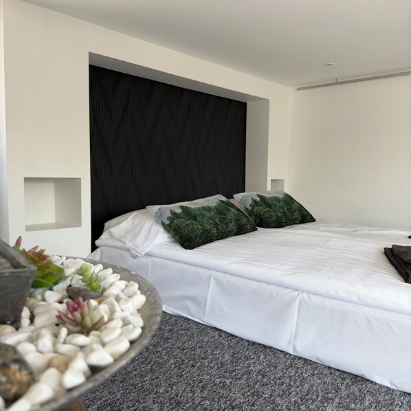 A modern bedroom with a large bed, a dark headboard, and a small bedside table with a plant. - Ringö Resort (Gothenburg)