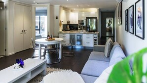 Eine moderne Küche mit einer zentralen Kochinsel, einem Essbereich mit rundem Tisch und einem Wohnbereich mit Sofa und Fernseher.