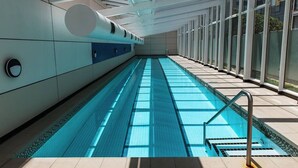 Ein langer, überdachter Pool mit klarem, blauem Wasser, gefliesten Wänden und modernem architektonischen Design.