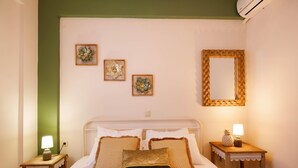 A neatly made bed with a white headboard, two bedside tables with lamps, and three framed artworks on the wall. - Green A Seaside Escape With Mesmerizing Views (Rethymno)