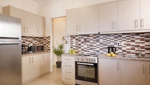A modern kitchen with a refrigerator, microwave, stove, and sink. There is a potted plant and a coffee maker on the counter. - Green A Seaside Escape With Mesmerizing Views (Rethymno)