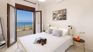Quarto com cama, mesa de cabeceira, janela com vista para o mar e ar condicionado.