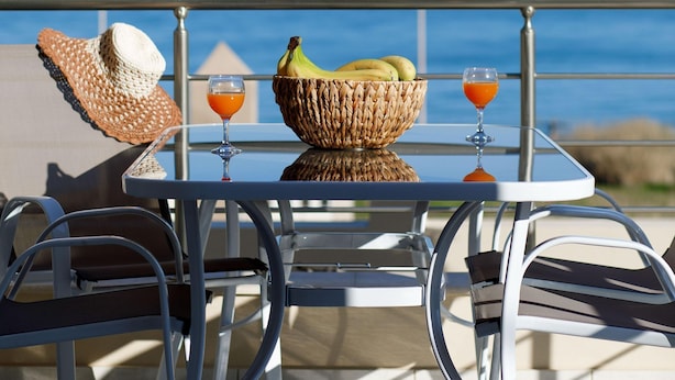 Uma mesa com uma cesta de palha, dois copos de suco de laranja e um chapéu de palha numa varanda com vista para o mar.