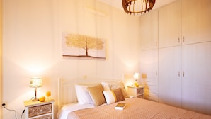 Et soveværelse med seng, sengeborde, en lampe, et billede af et træ og et garderobeskab.