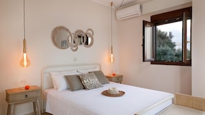 A neatly arranged bedroom with a bed, bedside tables, a woven basket, and a window with a view. - Peach- Sea View Exclusive Maisonette (Rethymno)