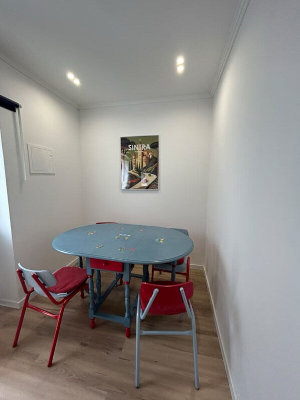 Una habitación con una mesa redonda y cuatro sillas, un cartel en la pared y un interruptor de luz.