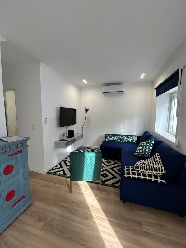 Una sala de estar moderna con un sofá azul, una mesita, un televisor y un aparador decorativo.
