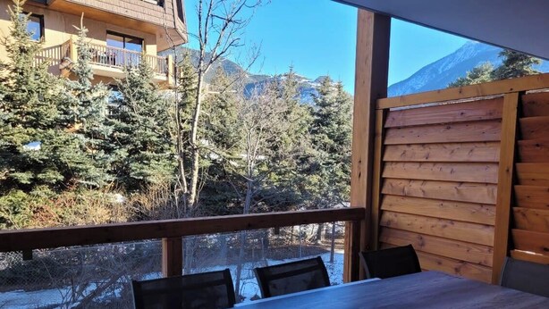 Une terrasse en bois avec une table et des chaises, donnant sur un paysage enneigé parsemé d’arbres et de montagnes.